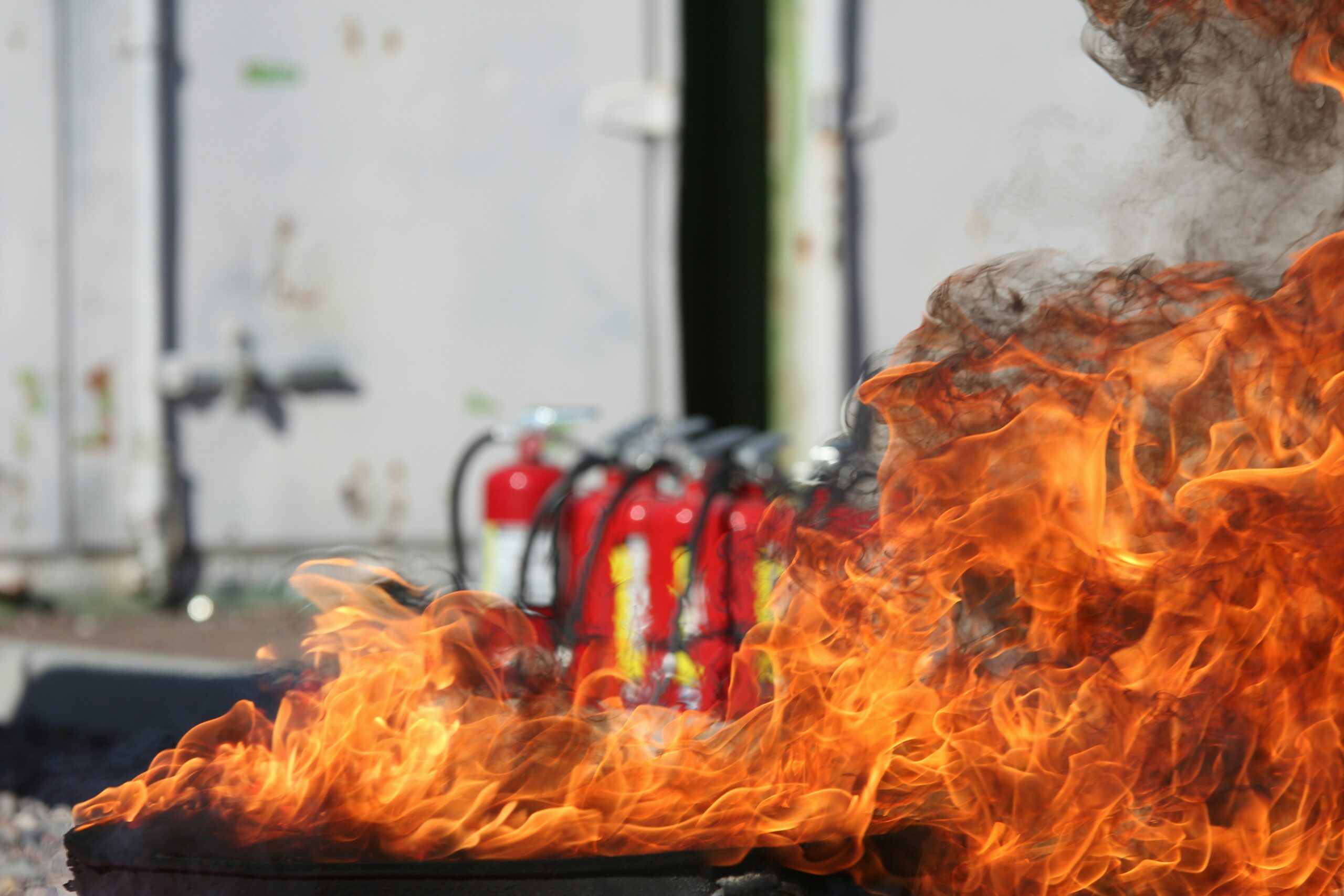 flames from a fire with several red fire extinguishers in the background
